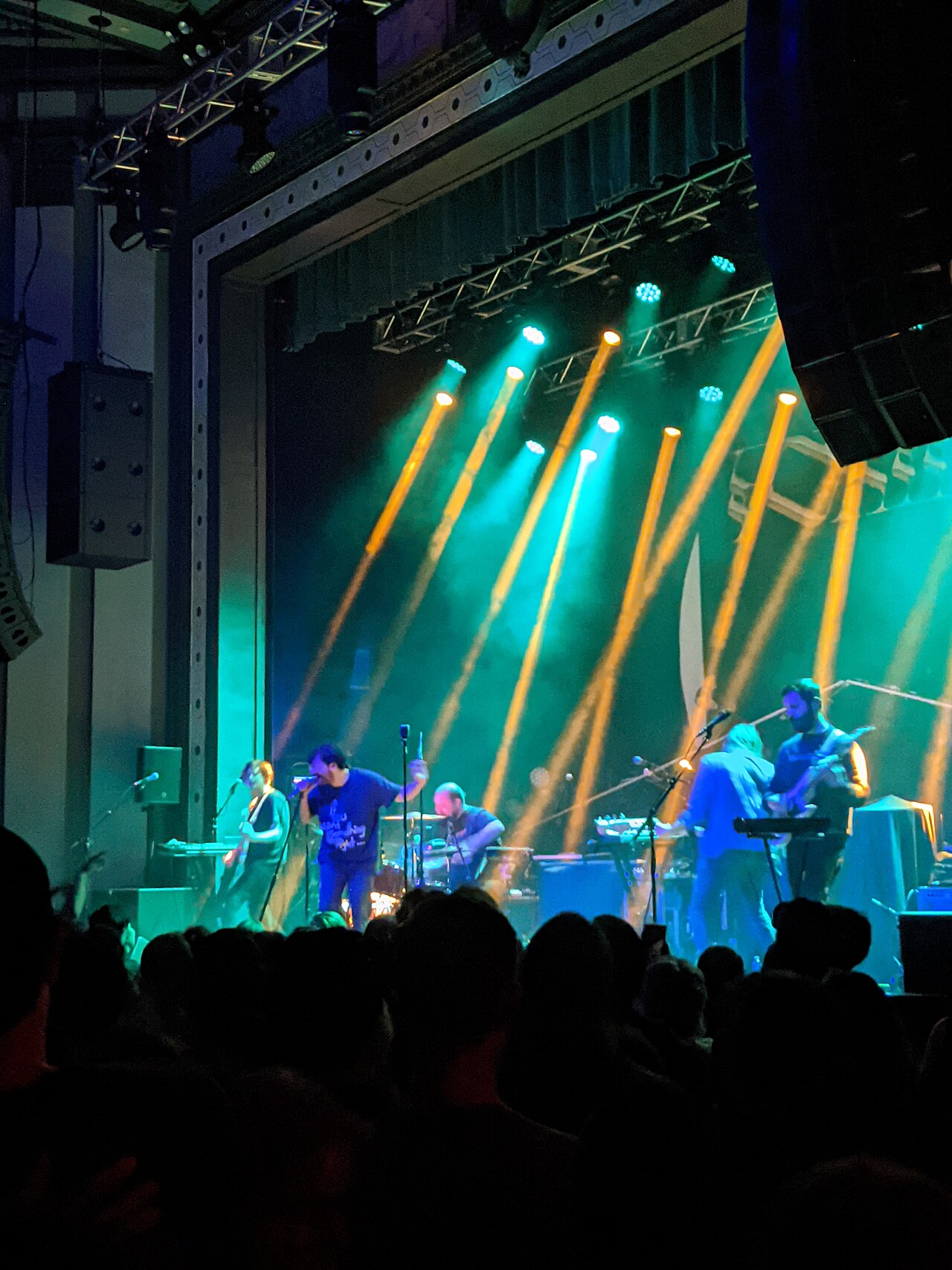 An indie band playing an intimate show in a dimly lit club, a spotlight on the lead singer, audience visible.
